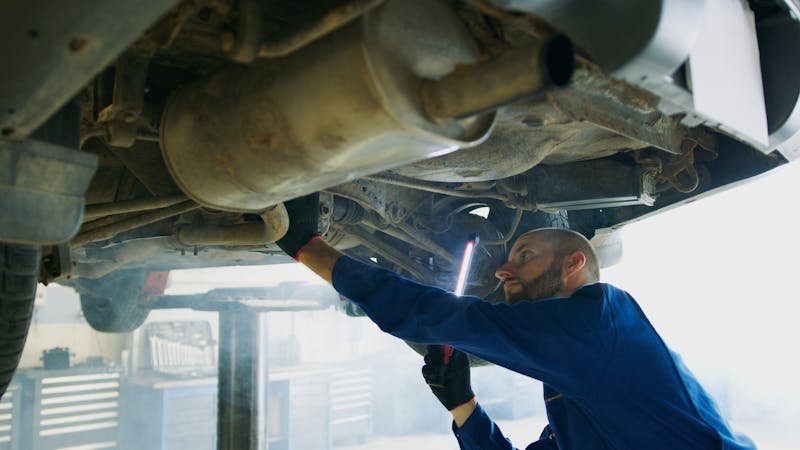 Mechanic inspecting exhaust and DPF system underneath a vehicle