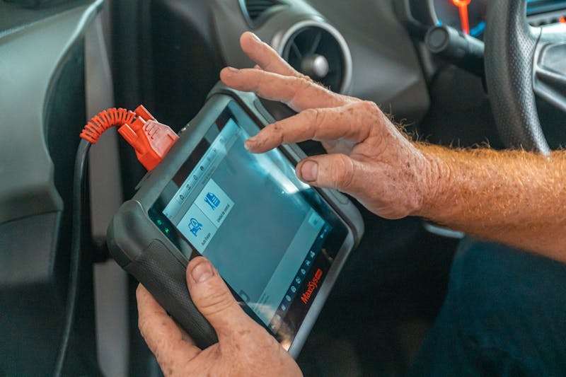 Mechanic using diagnostic tablet tool inside a vehicle
